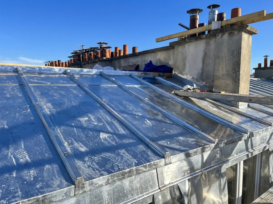 Deux couvreurs professionnels travaillent sur une toiture en chantier au coucher du soleil
