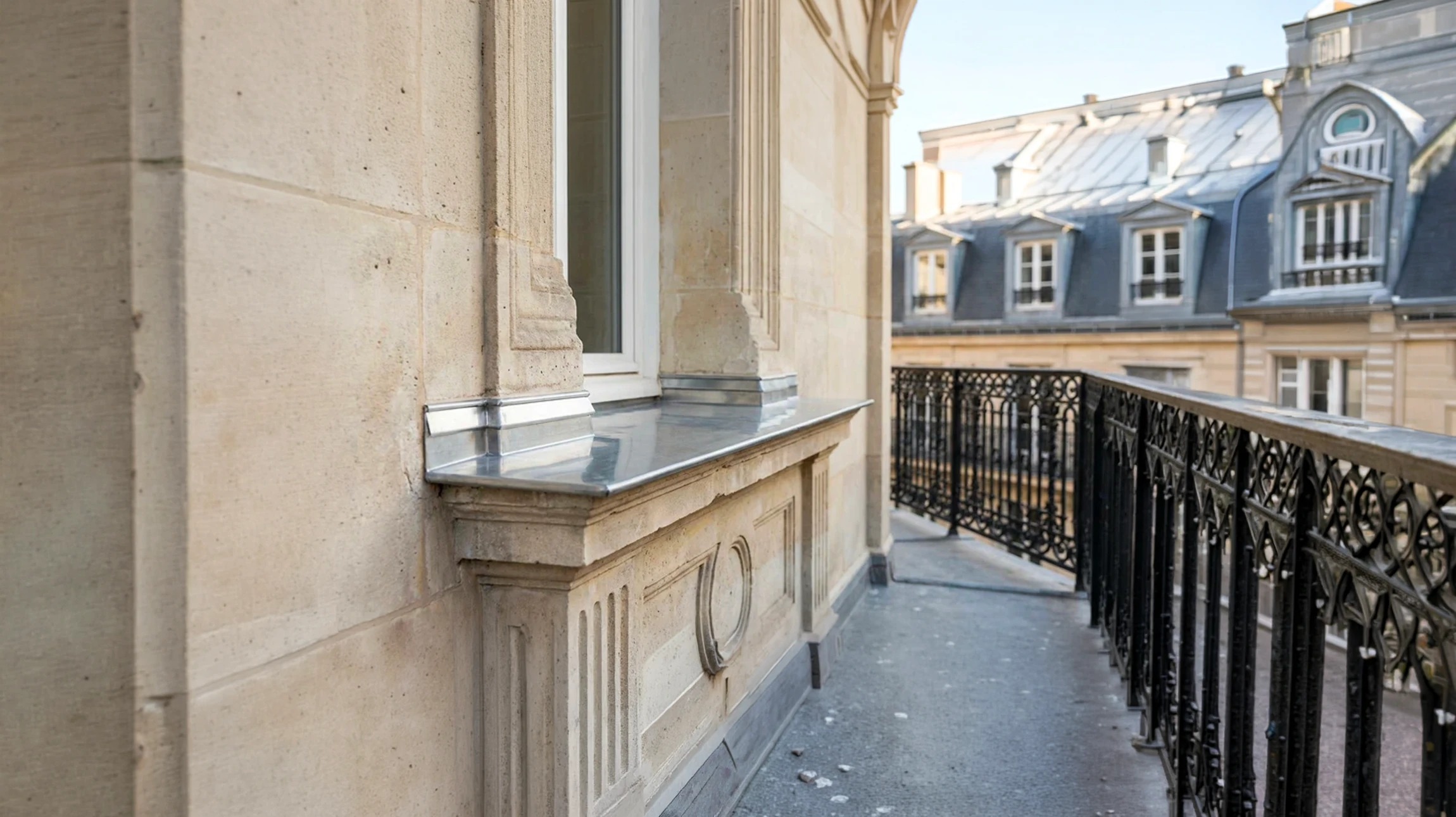 Gros plan professionnel d'un appui de fenêtre en zinc brillant, fraîchement rénové, installé sur la façade en pierre d'un immeuble haussmannien parisien. On voit nettement les détails du zinc poli avec ses reflets, la jonction avec la maçonnerie, et en arrière-plan légèrement flou la façade historique de l'immeuble. La photo est prise de jour en lumière naturelle, montrant la qualité de finition et l'élégance du matériau noble.