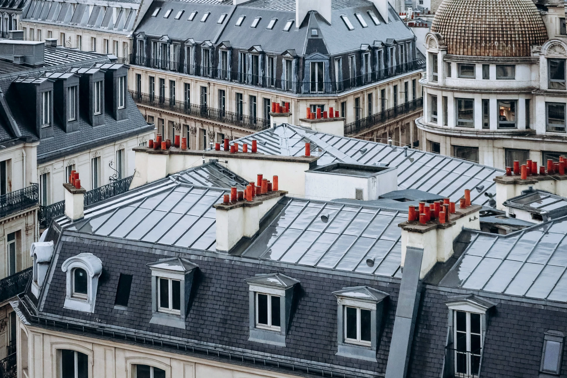 Photographie réaliste d'une toiture haussmannienne parisienne en tuiles ou ardoise, présentant des signes visibles de fuite ou d'infiltration d'eau : zone humide sur les tuiles, trace d'eau suintant, détérioration locale ou moisissure, capturée de manière à montrer l'urgence d'une intervention. Lumière naturelle, prise de vue suffisamment large pour contexte urbain parisien typique.