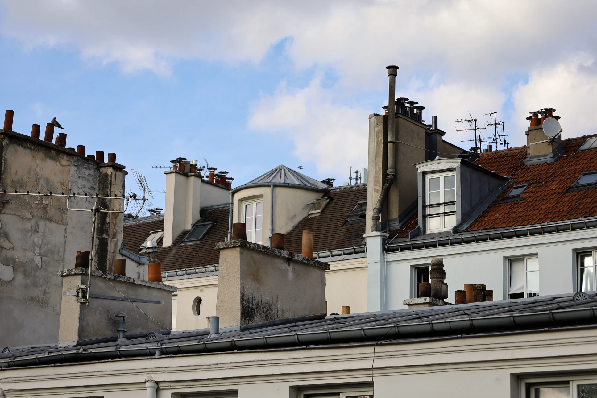 Extérieur d'une habitation avec cheminée en briques brunes à joints blancs, surmontée d'un chapeau en béton et conduit métallique