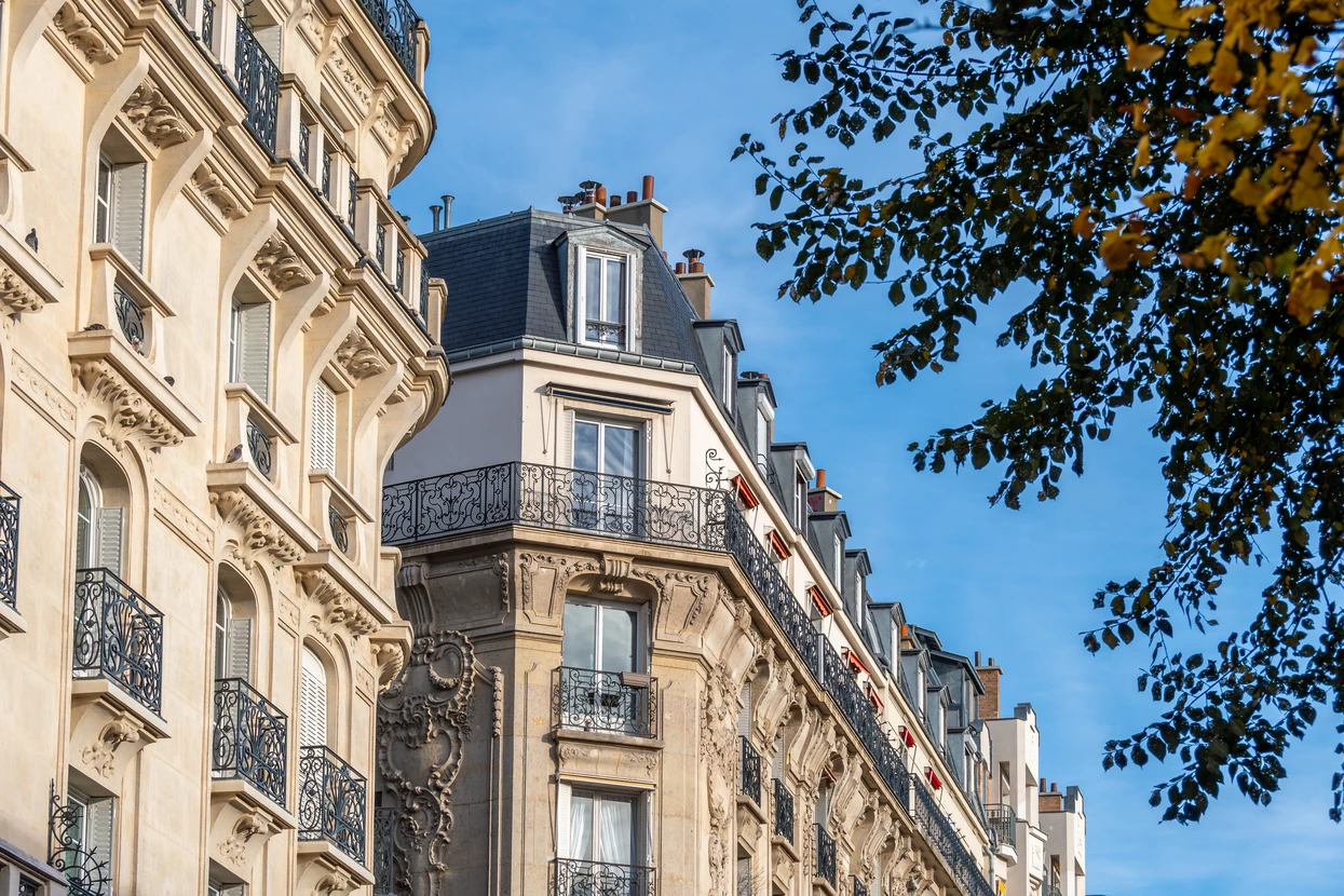 Façade d'immeuble haussmannien parisien en pierre de taille beige avec balcons en fer forgé