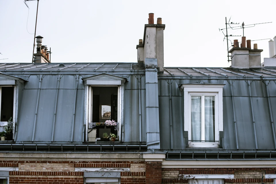 Ouvrier en combinaison de protection int&eacute;grale blanche travaillant sur toiture en ardoises, utilisant une &eacute;chelle aluminium pour acc&eacute;der aux tuiles d&eacute;faillantes