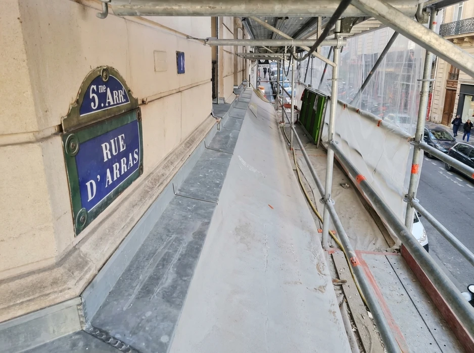 Couvreur professionnel travaillant sur toiture en tuiles métalliques, utilisant une échelle de toit pour accéder à une cheminée en briques