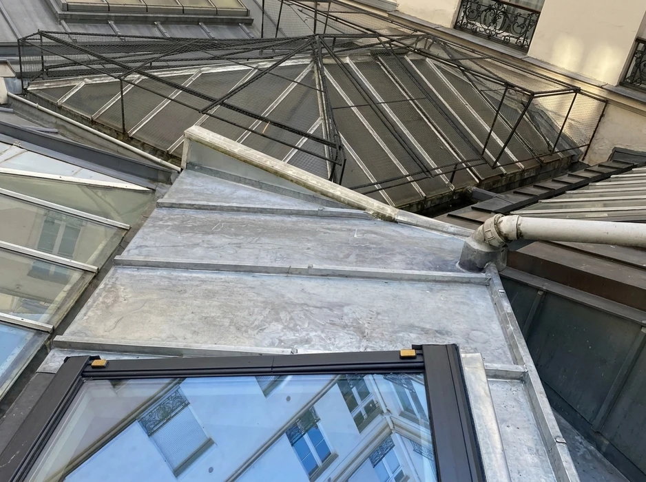 Cheminée en briques anciennes sur toiture résidentielle, extérieur jour ensoleillé, arbres en arrière-plan, ciel bleu dégagé