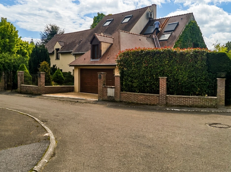 Couvreur professionnel travaillant sur toiture en tuiles métalliques, utilisant une échelle de toit pour accéder à une cheminée en briques
