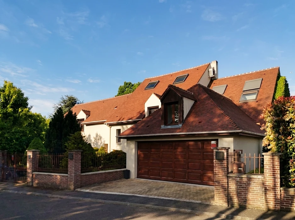 Cheminée en briques anciennes sur toiture résidentielle, extérieur jour ensoleillé, arbres en arrière-plan, ciel bleu dégagé