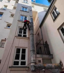 Échafaudage métallique tubulaire installé le long d'une toiture mansardée en zinc, vue en hauteur sur toits parisiens