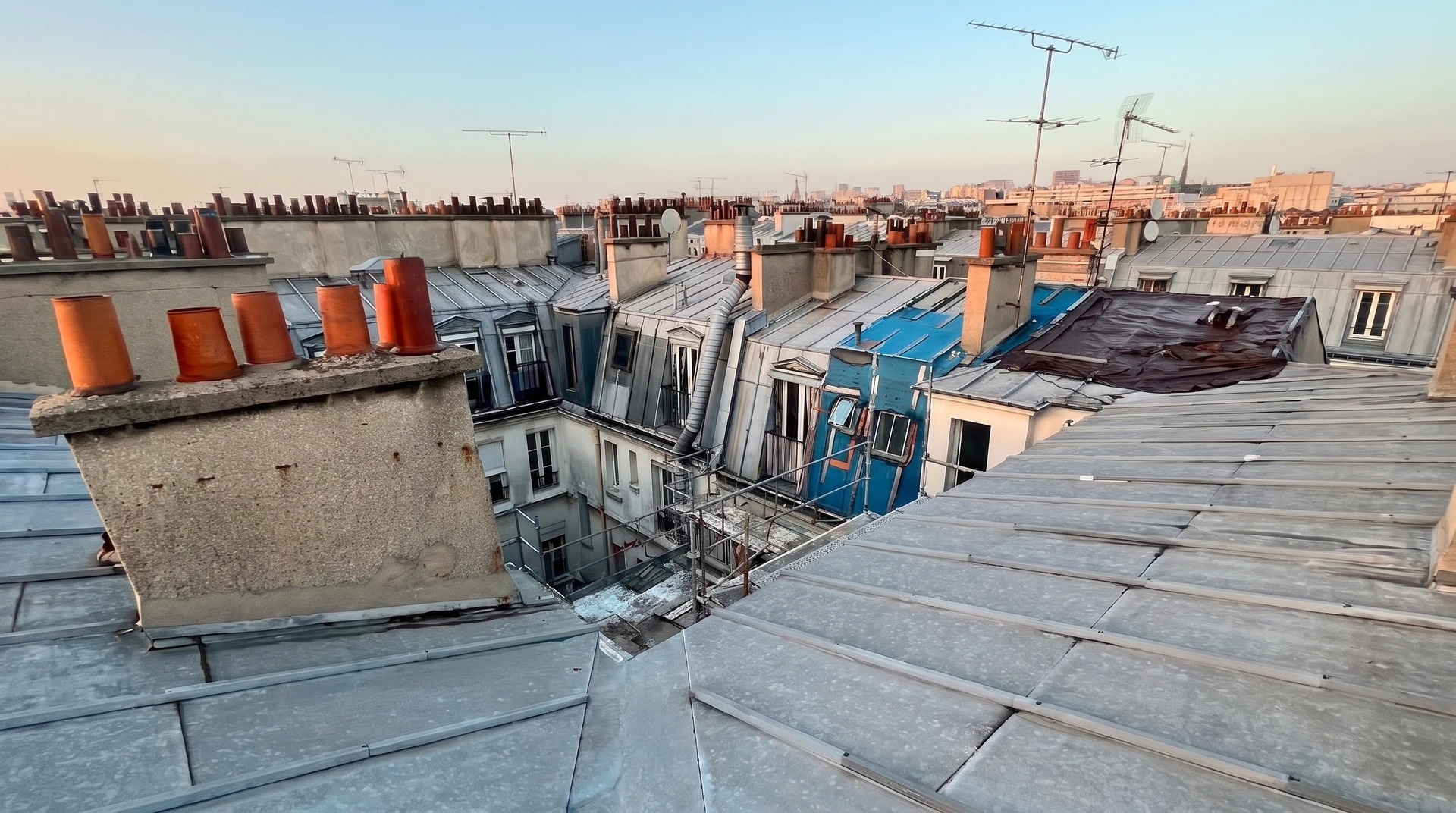 Cordiste en rappel sur corde équipé d'un harnais de sécurité et d'un casque, intervenant sur la toiture en zinc à joints debout d'un immeuble haussmannien parisien, effectuant des travaux d'étanchéité ou de réparation, avec fond urbain parisien visible, aucun échafaudage n'étant installé au sol.